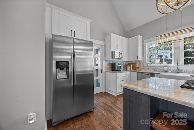 kitchen with vaulted ceiling, appliances with stainless steel finishes, light stone counters, and white cabinetry