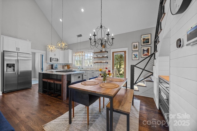 dining room with high vaulted ceiling, dark wood finished floors, an inviting chandelier, and stairs