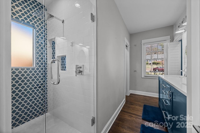 bathroom with wood finished floors, a shower stall, vanity, and baseboards