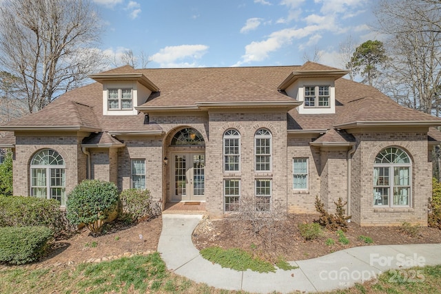 french country home with french doors, brick siding, and roof with shingles