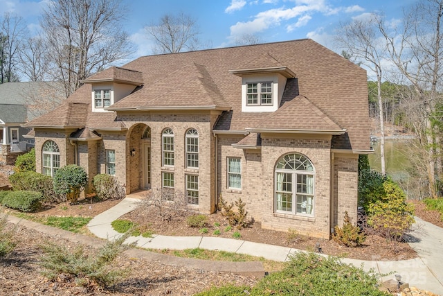 french provincial home featuring brick siding and roof with shingles