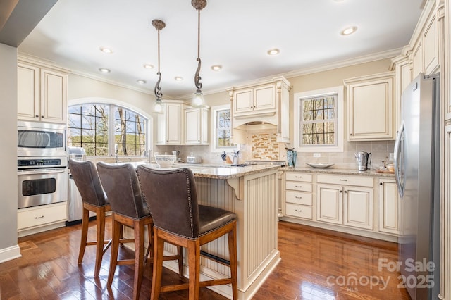 kitchen with cream cabinetry, tasteful backsplash, hardwood / wood-style floors, appliances with stainless steel finishes, and light stone countertops