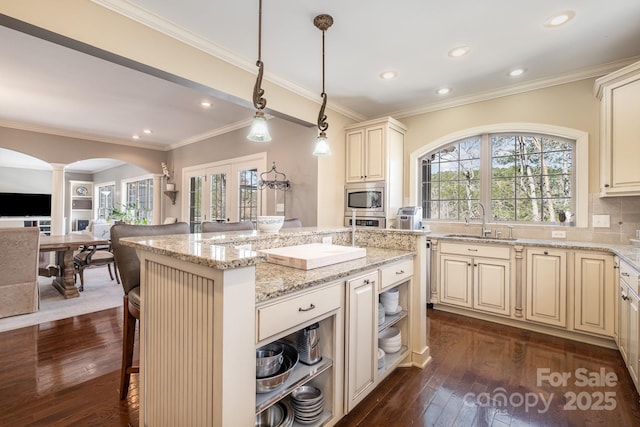 kitchen featuring ornate columns, arched walkways, a sink, cream cabinetry, and appliances with stainless steel finishes