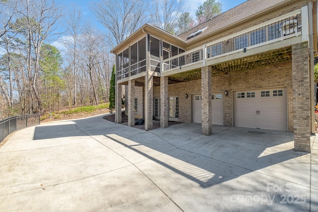 view of side of property featuring driveway, an attached garage, a sunroom, french doors, and brick siding