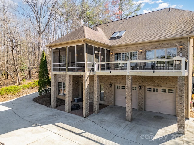 back of house featuring brick siding, a shingled roof, concrete driveway, a sunroom, and an attached garage