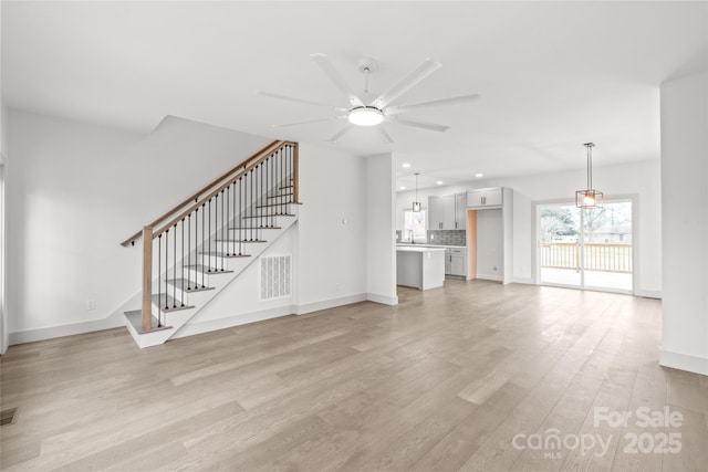 unfurnished living room featuring stairway, light wood-style flooring, visible vents, and ceiling fan