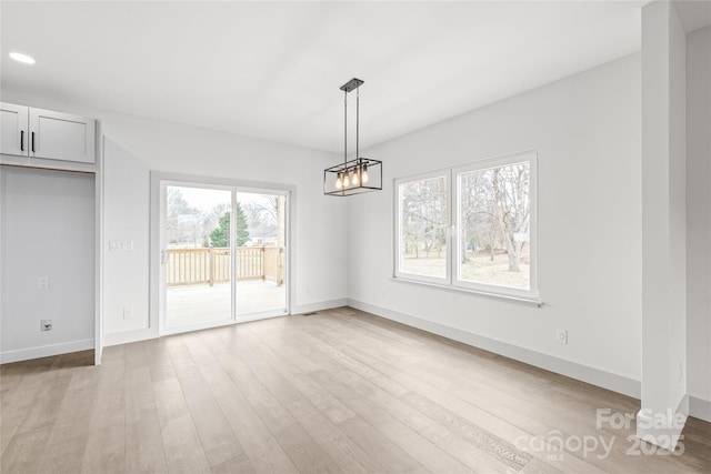 unfurnished dining area featuring light wood-type flooring, an inviting chandelier, and baseboards