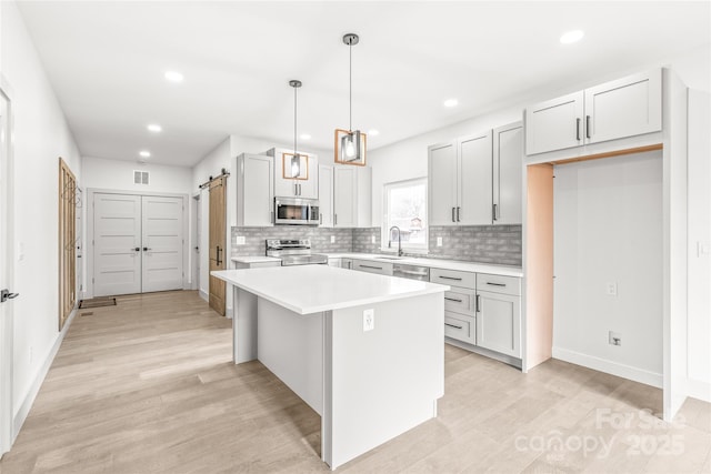 kitchen featuring stainless steel appliances, visible vents, light countertops, a center island, and light wood finished floors