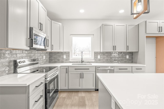 kitchen featuring stainless steel appliances, light countertops, backsplash, a sink, and light wood-type flooring