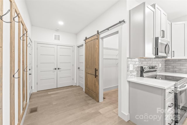 kitchen with stainless steel appliances, a barn door, light countertops, and visible vents