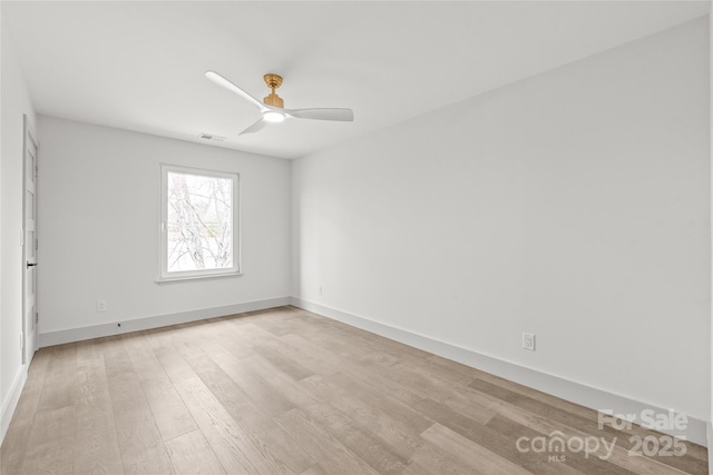 empty room with visible vents, light wood-type flooring, a ceiling fan, and baseboards