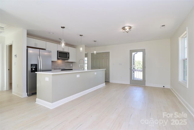 kitchen featuring a center island with sink, stainless steel appliances, light countertops, light wood-type flooring, and backsplash