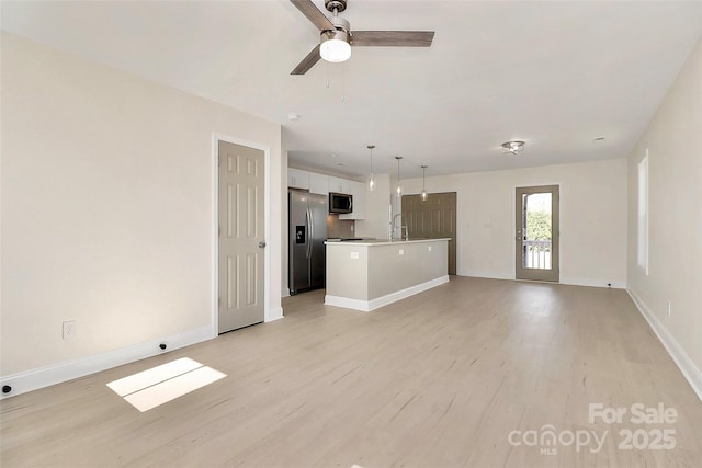 unfurnished living room with a ceiling fan, a sink, light wood-style flooring, and baseboards