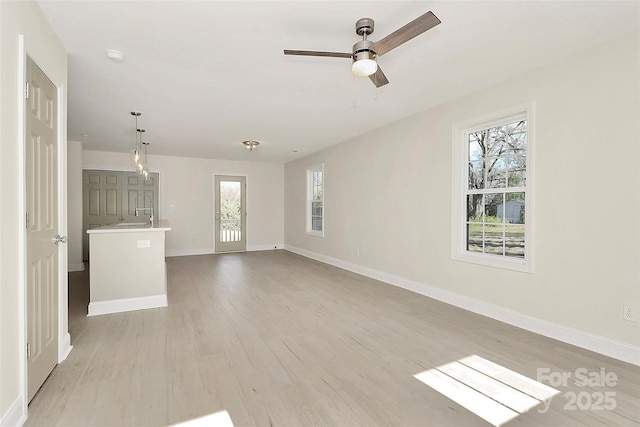 unfurnished living room with light wood-style floors, a sink, ceiling fan, and baseboards