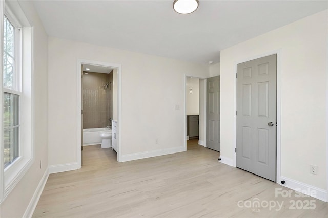 unfurnished bedroom with light wood-style floors, connected bathroom, and baseboards