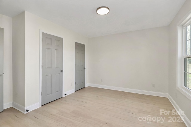 unfurnished bedroom with light wood-type flooring, multiple windows, and baseboards