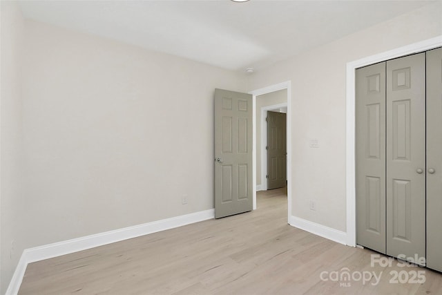 unfurnished bedroom featuring light wood-type flooring, baseboards, and a closet