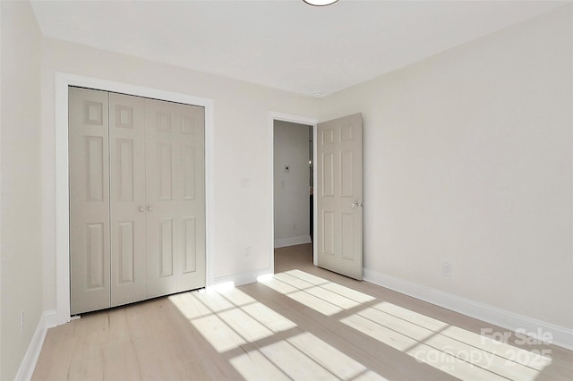 unfurnished bedroom with a closet, light wood-type flooring, and baseboards