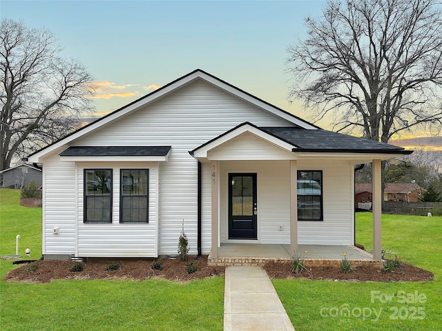 bungalow with a front yard, covered porch, and a shingled roof