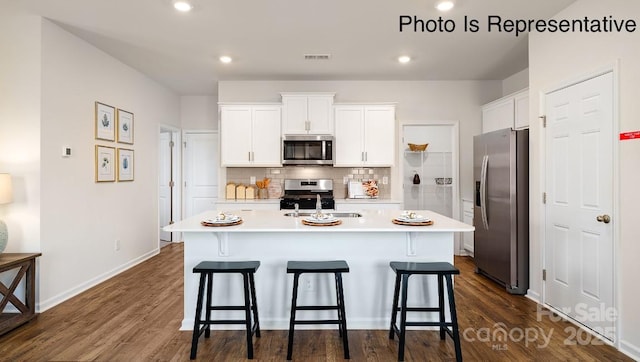 kitchen with a sink, light countertops, appliances with stainless steel finishes, a kitchen bar, and a center island with sink