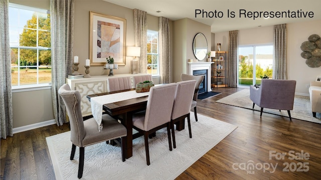 dining area featuring a fireplace with flush hearth, dark wood-style flooring, and baseboards