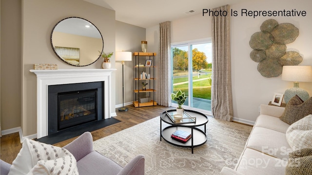 living room with a fireplace with flush hearth, visible vents, baseboards, and wood finished floors