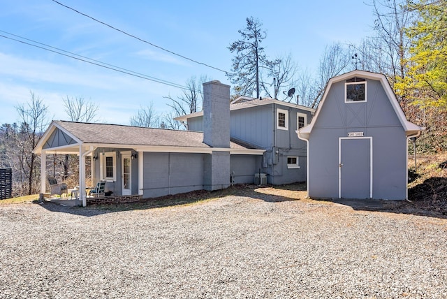 rear view of property with central AC unit, a chimney, roof with shingles, an outbuilding, and a porch