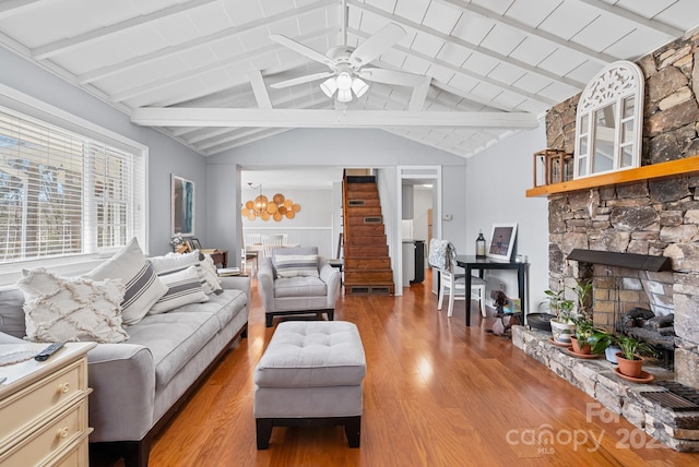 living room with vaulted ceiling with beams, ceiling fan, a stone fireplace, and light wood-style flooring