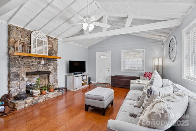 living room featuring lofted ceiling with beams, a ceiling fan, a stone fireplace, wood finished floors, and baseboards