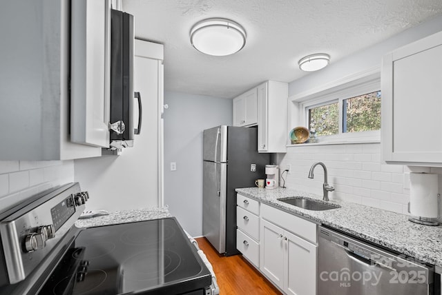 kitchen with light stone counters, stainless steel appliances, light wood-style flooring, white cabinets, and a sink