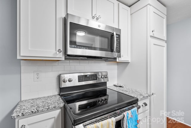 kitchen featuring white cabinets, light stone counters, stainless steel appliances, and decorative backsplash