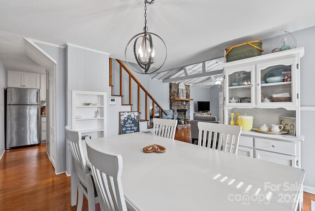 dining area with wood finished floors, a fireplace, an inviting chandelier, and stairs