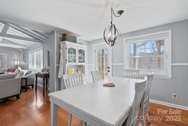 dining area with a chandelier, lofted ceiling with beams, and wood finished floors