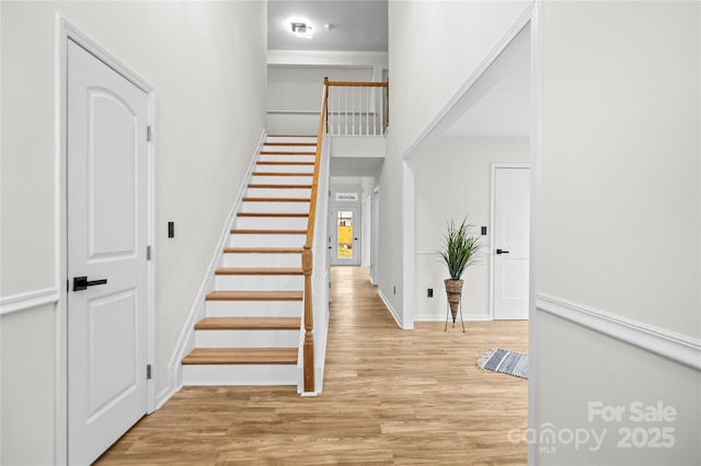 staircase featuring baseboards, a towering ceiling, and wood finished floors