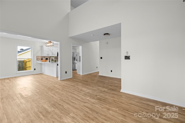 unfurnished living room featuring a sink, baseboards, light wood-style floors, and a towering ceiling