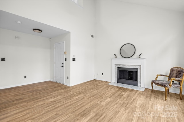 living area featuring visible vents, a high end fireplace, light wood-style floors, a high ceiling, and baseboards