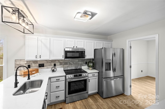 kitchen with a sink, stainless steel appliances, tasteful backsplash, and white cabinets