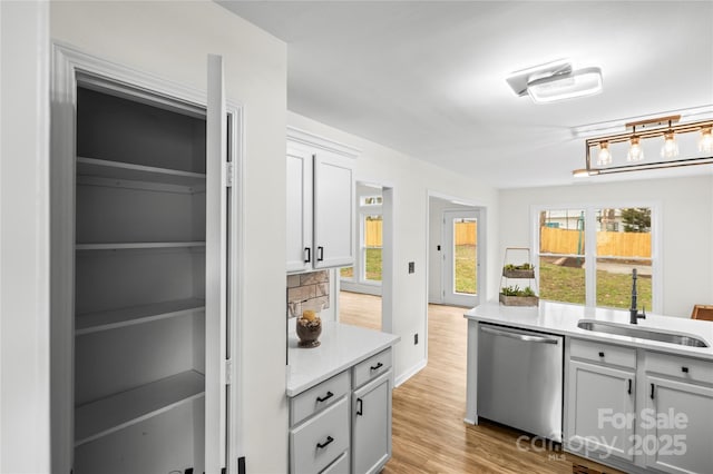 kitchen with stainless steel dishwasher, a healthy amount of sunlight, light wood finished floors, and a sink