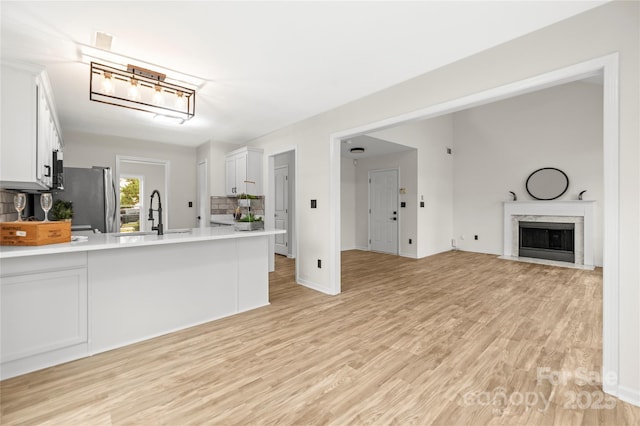 kitchen featuring light wood-type flooring, a sink, white cabinetry, freestanding refrigerator, and light countertops