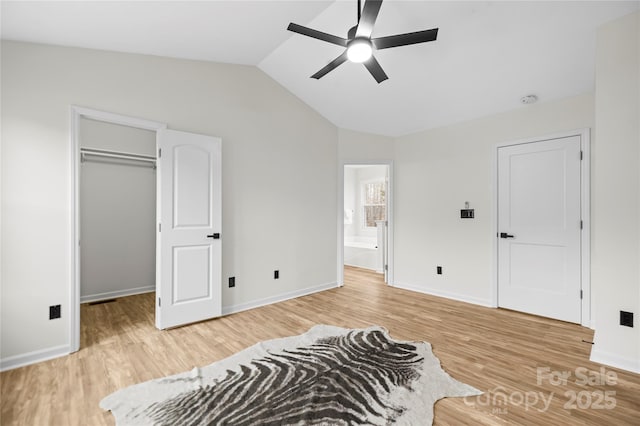 bedroom with a walk in closet, light wood-type flooring, and vaulted ceiling