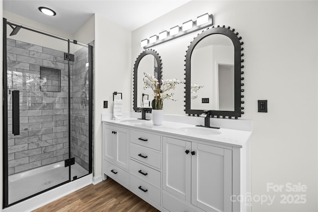 full bathroom featuring a shower stall, wood finished floors, double vanity, and a sink