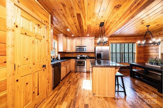 kitchen with light wood finished floors, appliances with stainless steel finishes, a center island, an inviting chandelier, and a sink