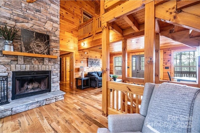 living room with wood walls, beamed ceiling, wood finished floors, and a stone fireplace