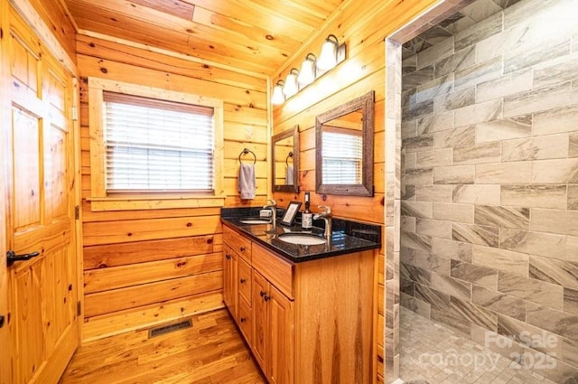 bathroom with wooden walls, visible vents, tiled shower, and wood finished floors