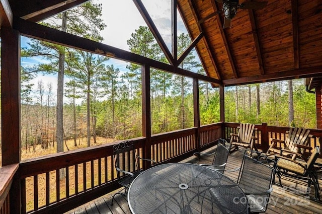 sunroom with lofted ceiling with beams, wooden ceiling, a ceiling fan, and a view of trees