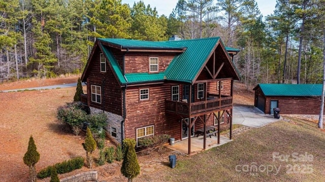 exterior space featuring an outbuilding, metal roof, a patio, stone siding, and a wooden deck