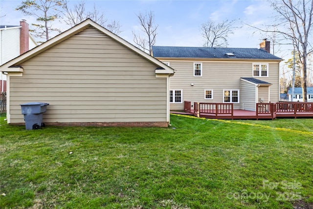 rear view of house with a chimney, a deck, and a lawn