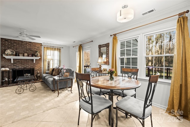 dining area with light tile patterned floors, visible vents, a ceiling fan, ornamental molding, and a fireplace