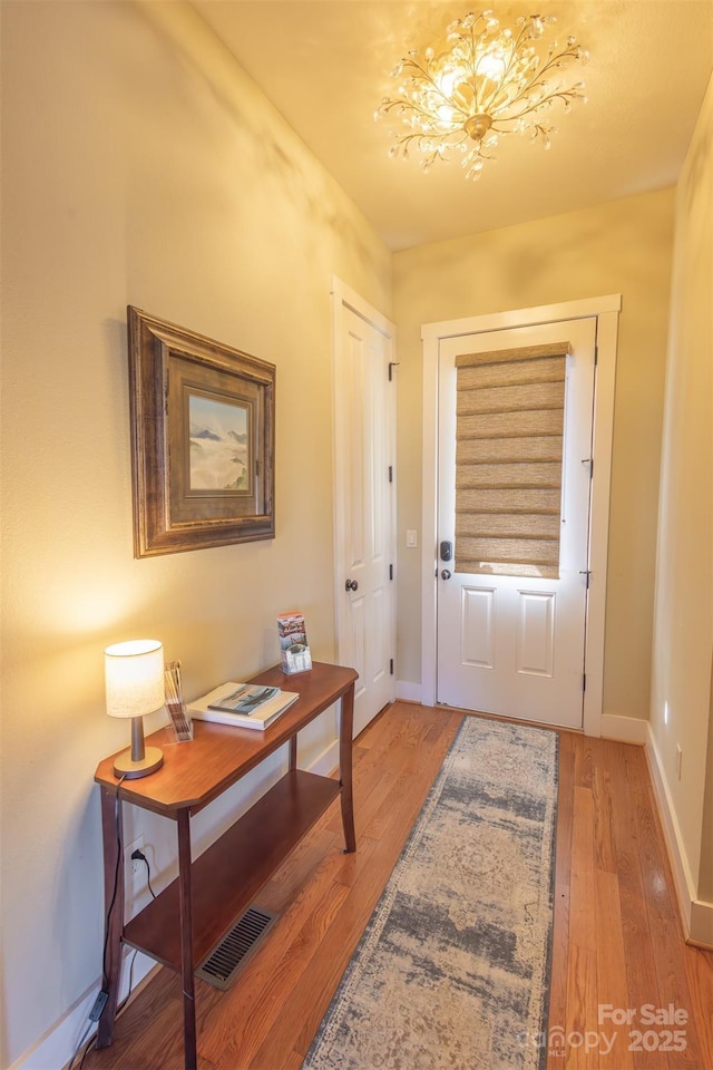 entryway featuring a notable chandelier, light wood-type flooring, visible vents, and baseboards