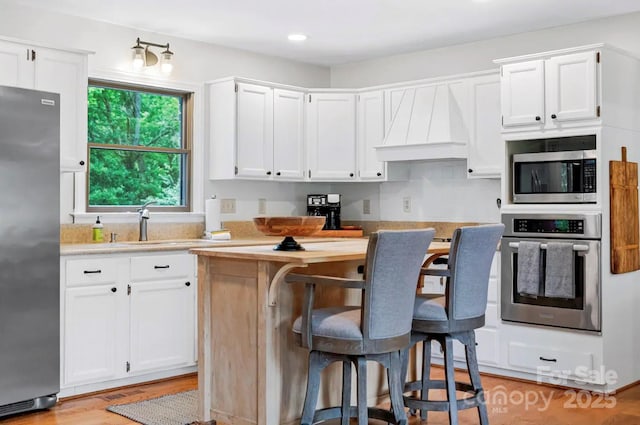 kitchen featuring custom exhaust hood, appliances with stainless steel finishes, white cabinets, and a center island